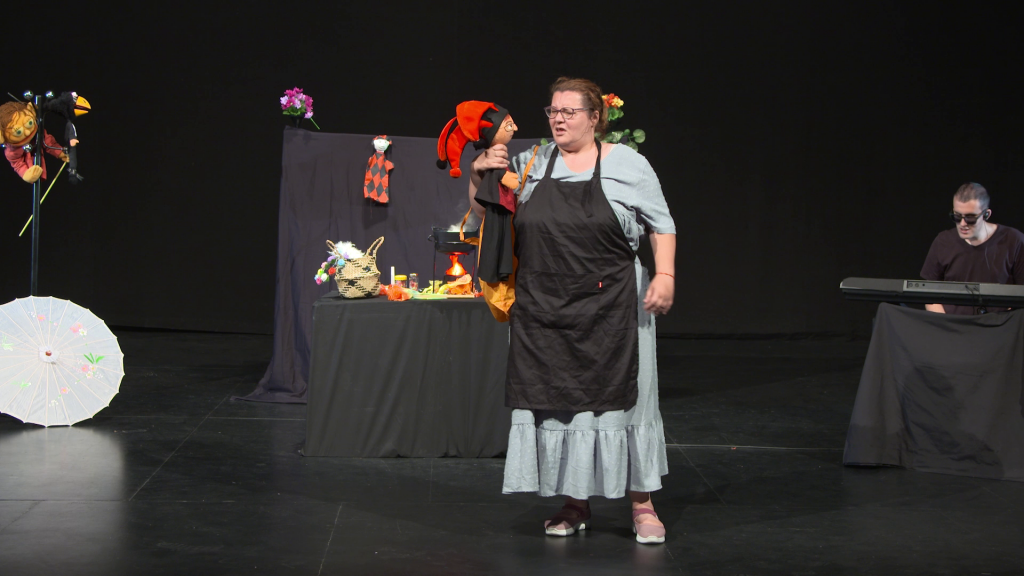 Escenario de la obra de teatro "Retablo de sueños"
Aparece la protagonista Julia con la marioneta Arlequín ante un decorado de cocina. A la derecha aparece un pianista ciego tocando.